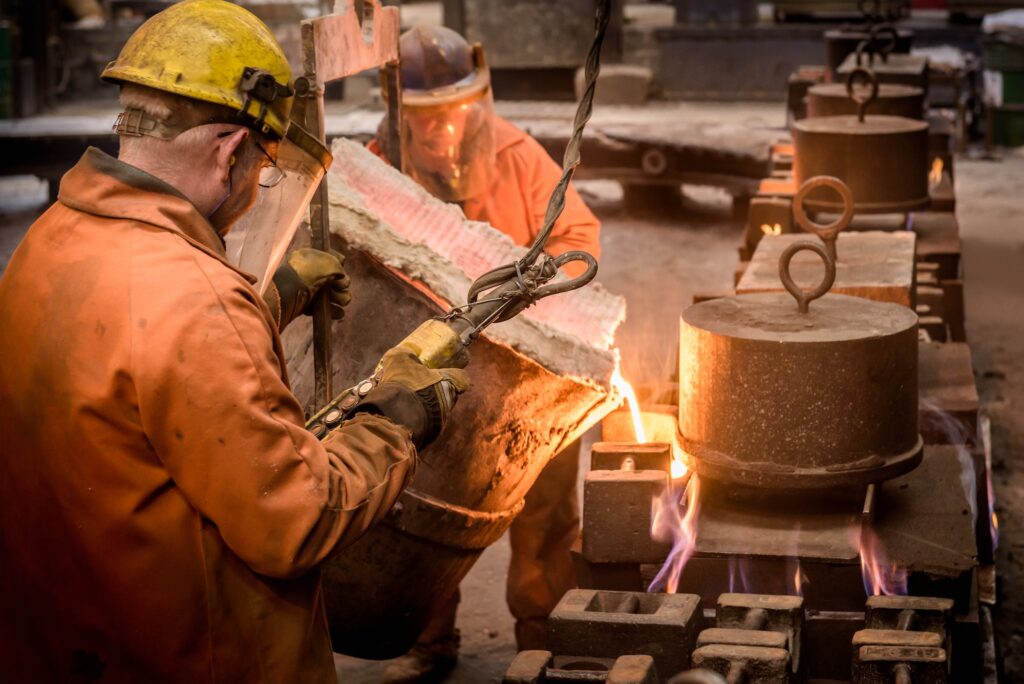 Workers pouring molten metal from flask in foundry