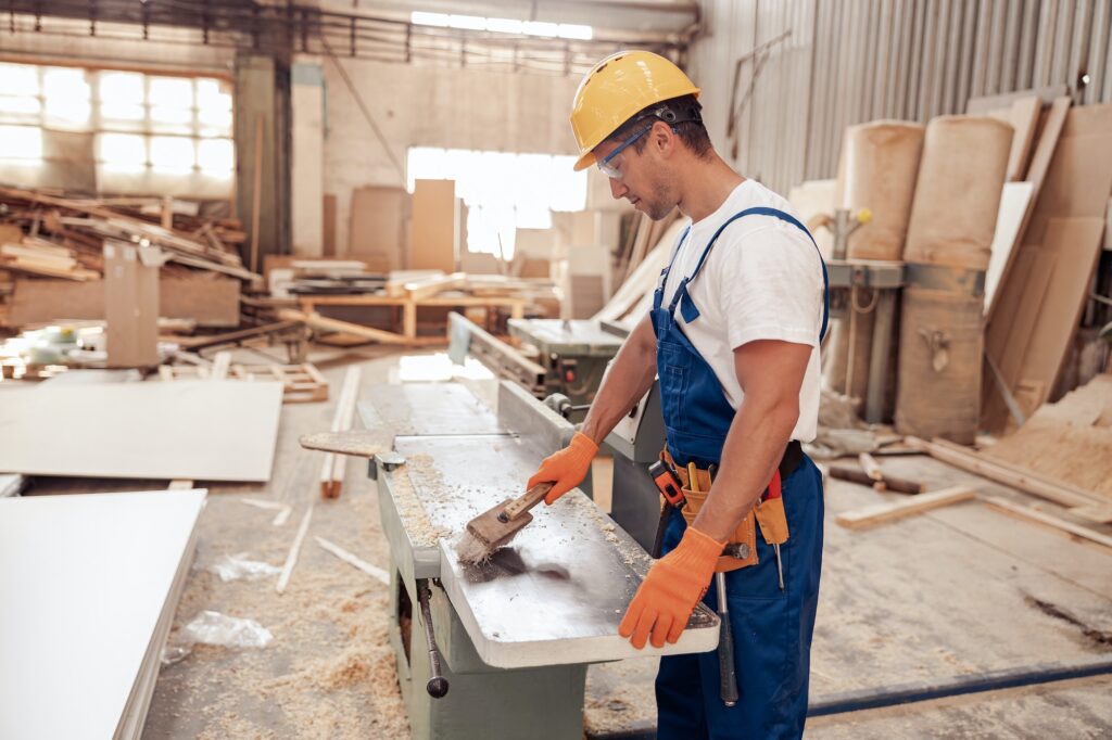 Male worker cleaning woodworking machine in workshop