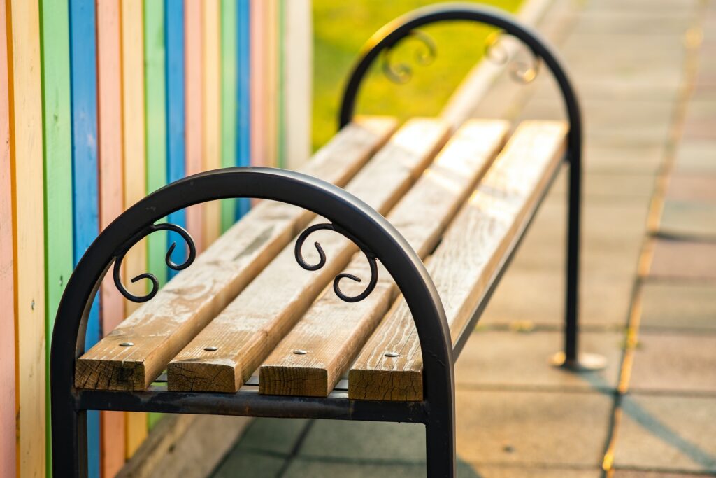 Closeup of wooden park bench with metal handgrip outdoors.