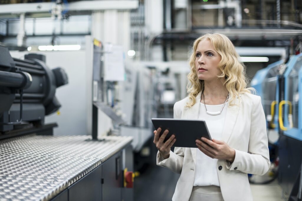 Woman with tablet at machine in factory shop floor looking around