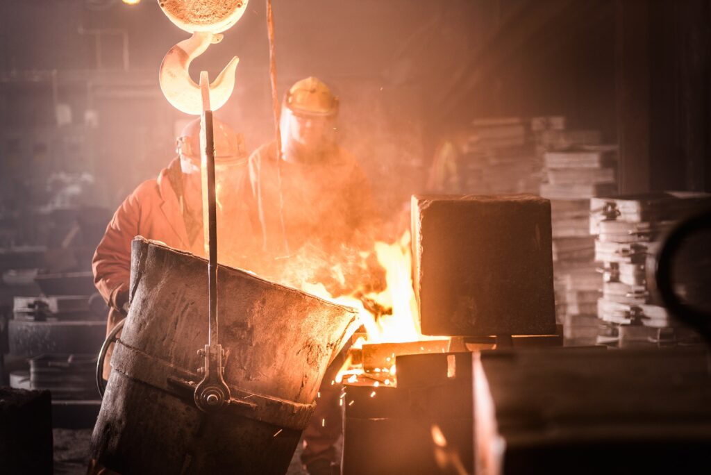 Workers pouring molten metal into moulds from flask in foundry