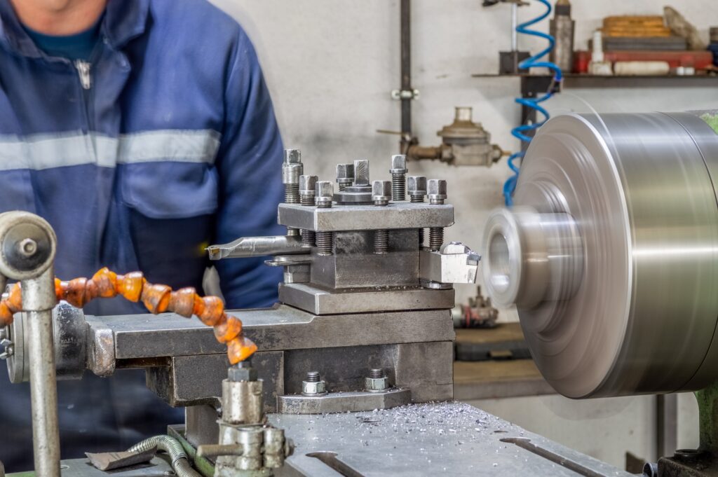 Blue-collar machine operator working with lathe machine in a factory.