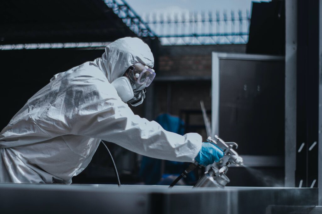 Person in protective coverall suit, goggles, and gas protection mask spray painting in a workshop