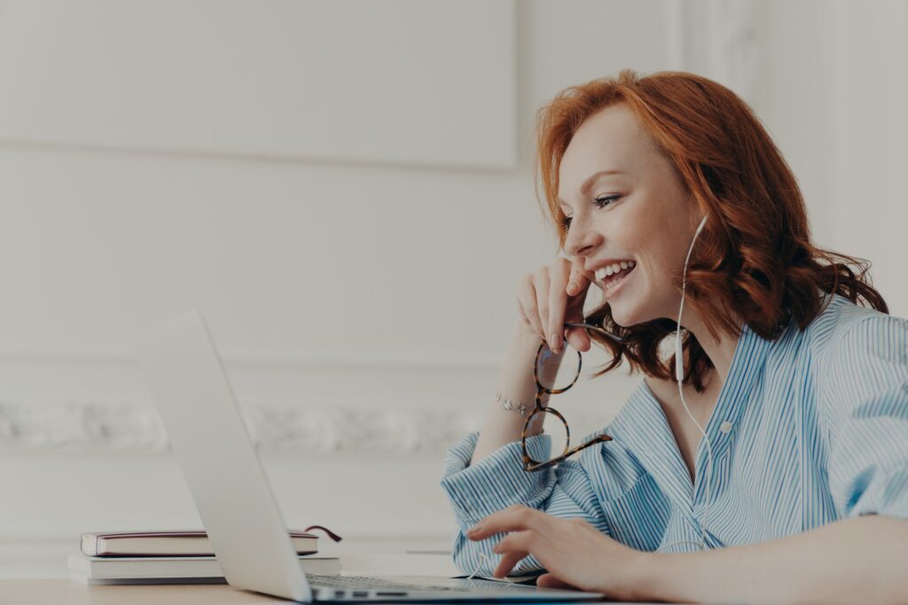 happy redhead woman laughs positively, has online communication with friend